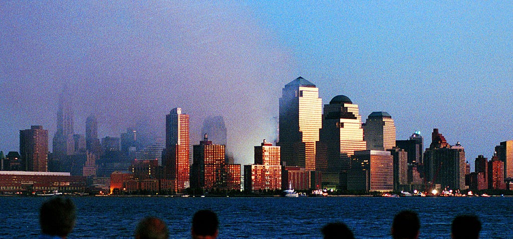People watch smoke rise from the former site of the World Trade Center on September 12, 2001, in Hoboken, New Jersey.